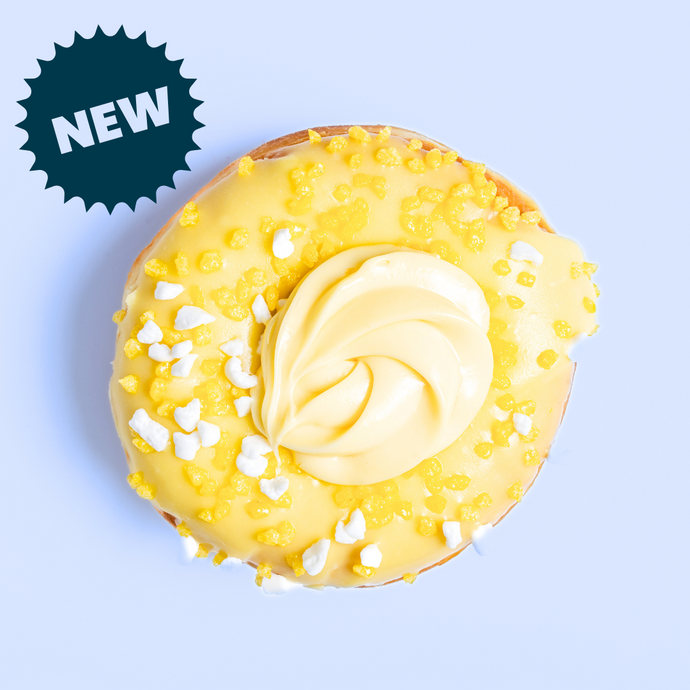 Lemon flavoured doughnut, with lemon creme, meringue pieces and lemon chunks on a light blue background and NEW label. 